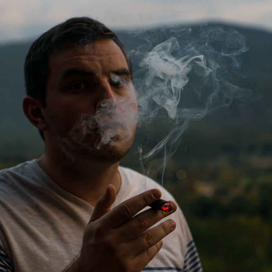 Man smoking ina field with mountains in the background 